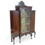 An Edwardian mahogany china cabinet with a carved upstand above an astragal glazed door flanked by