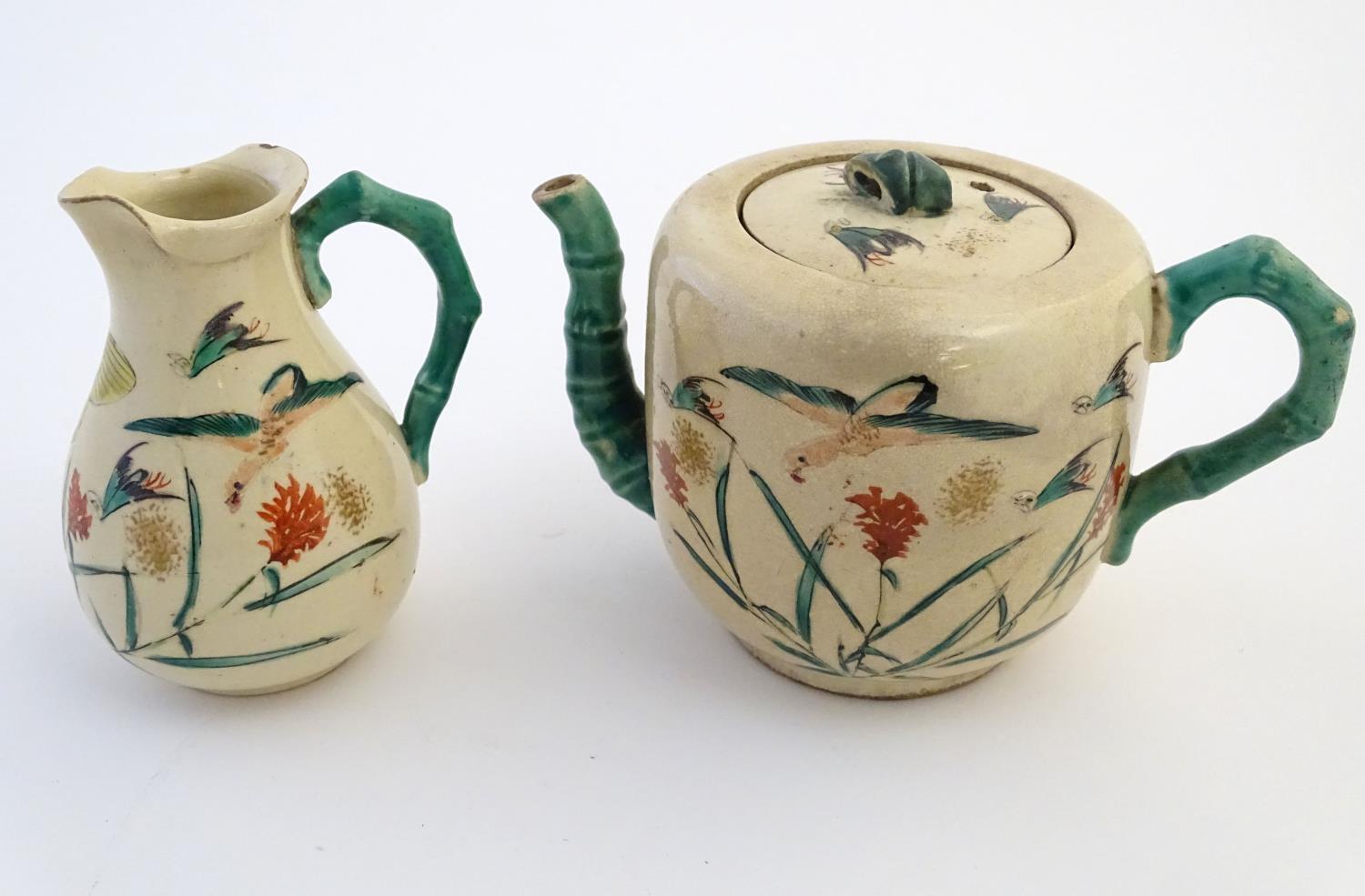 A Japanese teapot and milk jug with hand painted decoration depicting birds and flowers, the handles