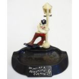 A mid 20thC novelty bakelite ashtray, decorated with an inebriated gentleman clinging to a lamp