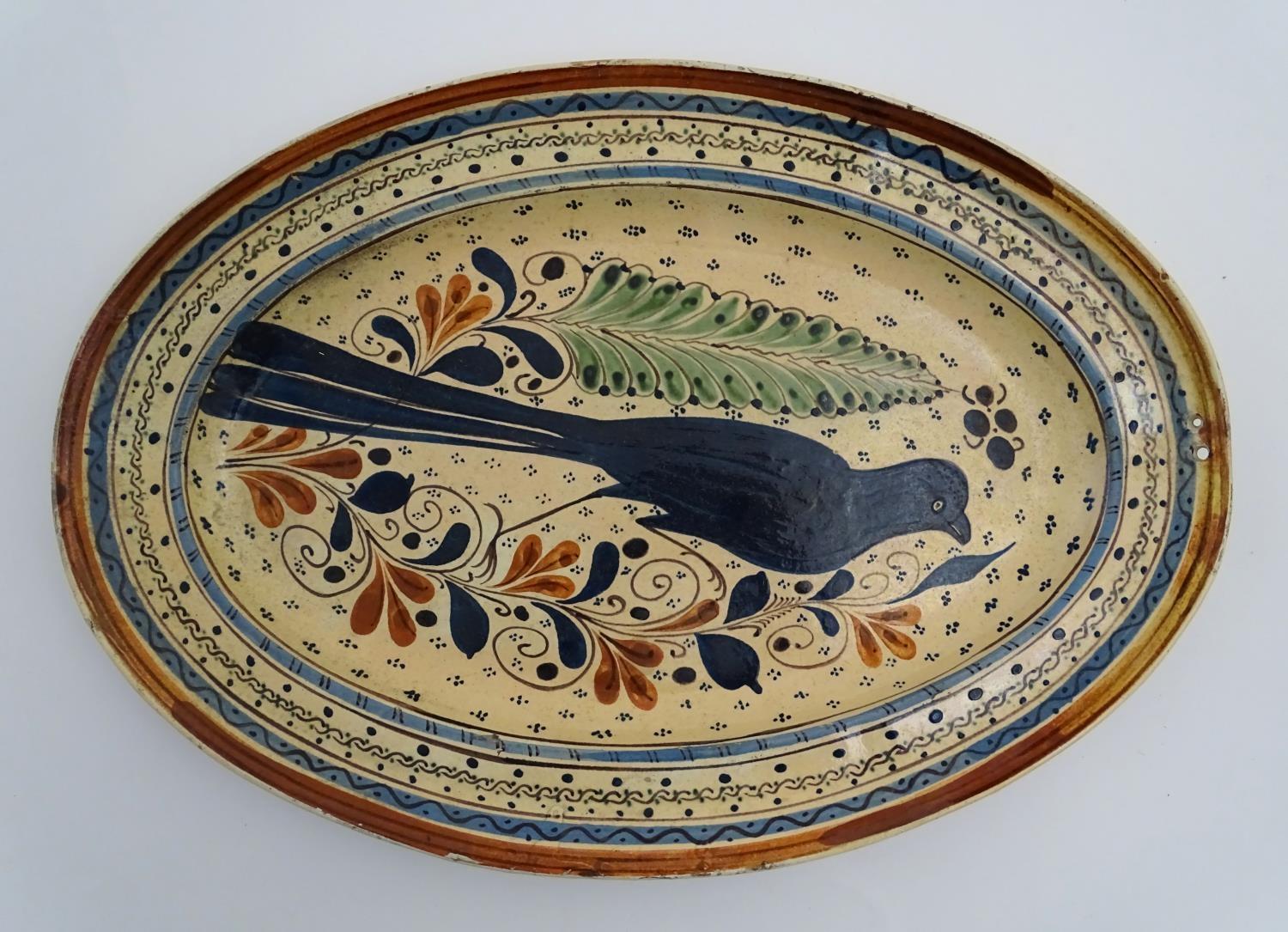 A Swiss terracotta oval pottery dish with hand painted folk art decoration depicting a bird