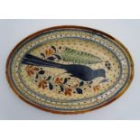 A Swiss terracotta oval pottery dish with hand painted folk art decoration depicting a bird