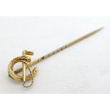 A yellow metal stick pin surmounted by horseshoe with riding whip decoration 2" long. Please