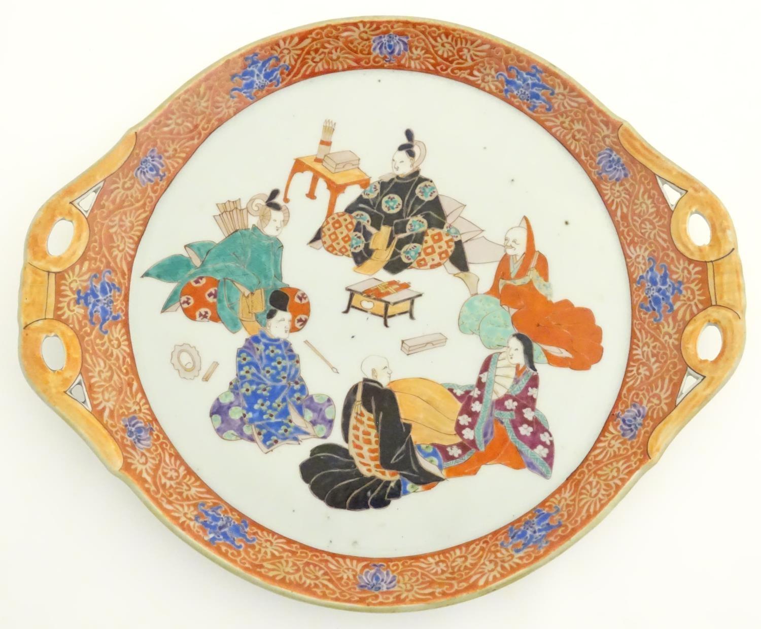 A Japanese twin handled plate with hand painted decoration depicting six seated figures with