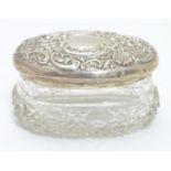 A cut glass dressing table pot of oval form with silver top having embossed decoration. Hallmarked