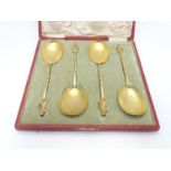 A cased set of four gilded serving spoons surmounted by a religious figure. Each approx. 8" long