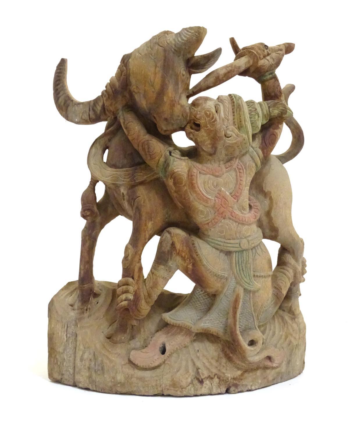 An Asian 20thC carved wooden sculpture modelled as a bull and warrior with polychrome decoration.
