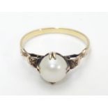 A yellow metal ring with claw set pearl and decorative shoulders. Ring size approx O Please Note -