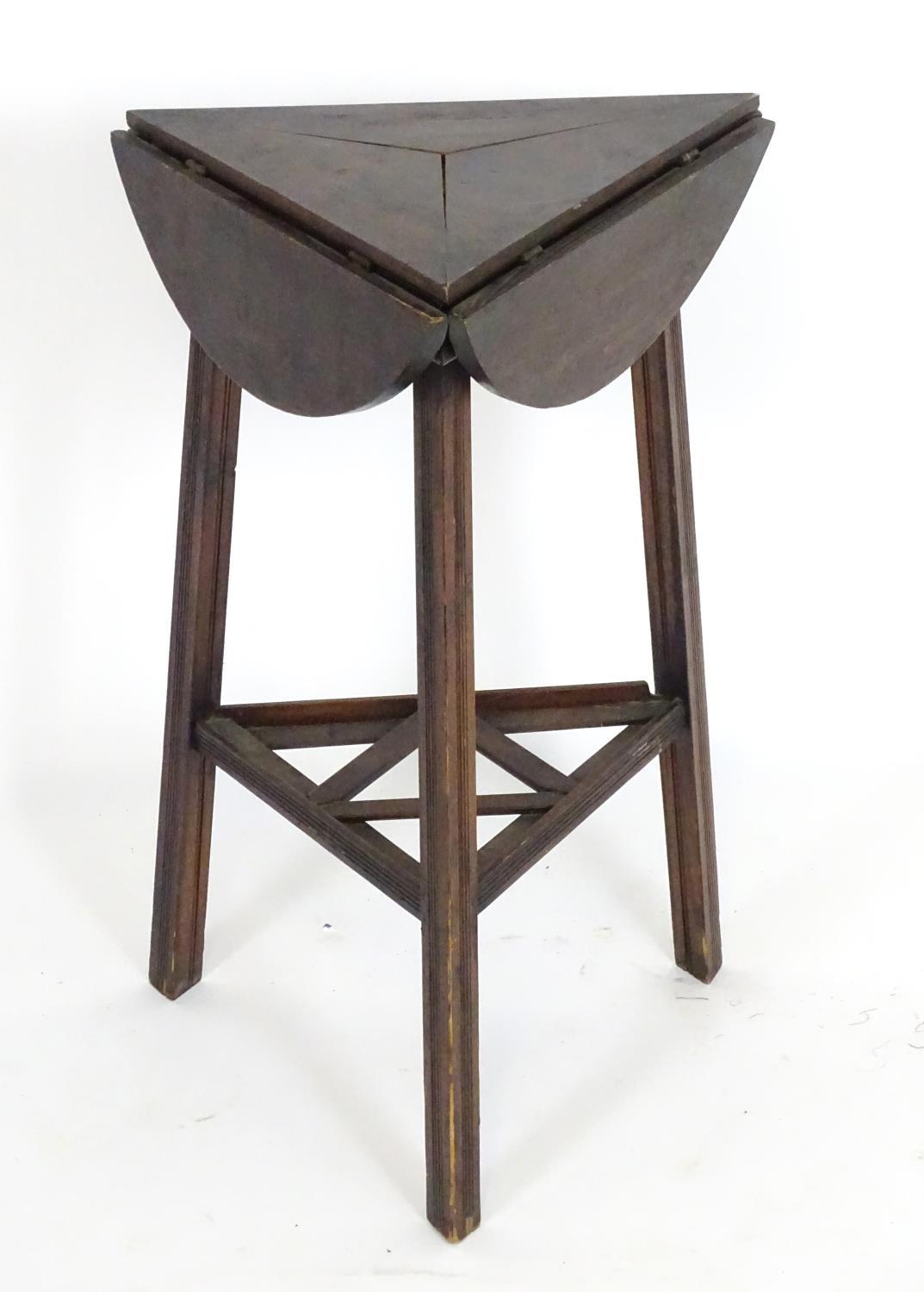An early 20thC country made cricket table with a folding rotating top and raised on three squared