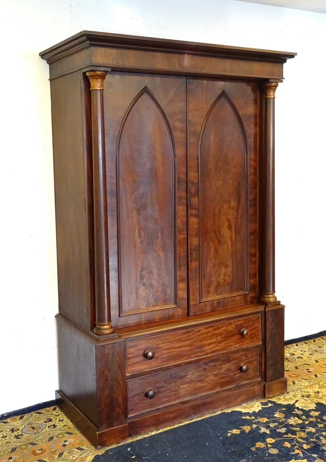 A 19thC mahogany press with a moulded cornice above two large doors with lancet shaped panelling,