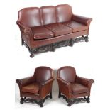 An early 20thC three piece leather suite with scrolled arms and carved legs united by shaped