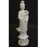 A Chinese blanc de chine figure of Guanyin standing holding flowers, raised on a base of lotus