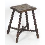 A late 19thC / early 20thC oak stool with floral carvings to the shaped top and standing on four