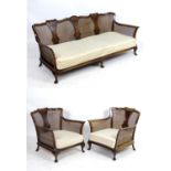 An early / mid 20thC bergere suite, comprising a sofa and two armchairs, having figured and shaped