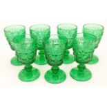 A set of 7 vintage green glass pedestal glasses with moulded decoration . Approx 4" high Please Note