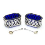A pair of silver salts with pierced decoration and blue glass liners, raised on four ball feet.