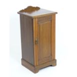 An early 20thC walnut bedside cabinet, with a shaped upstand and single fielded panelled door