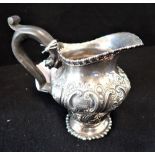 A SILVER CREAM JUG, embossed decorated, engraved with a crest, 10.5cm high (c.6.7oz)