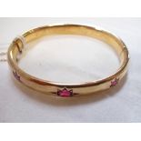 UNMARKED YELLOW METAL BANGLE, set with three 'garnets', concealed clasps and safety chain