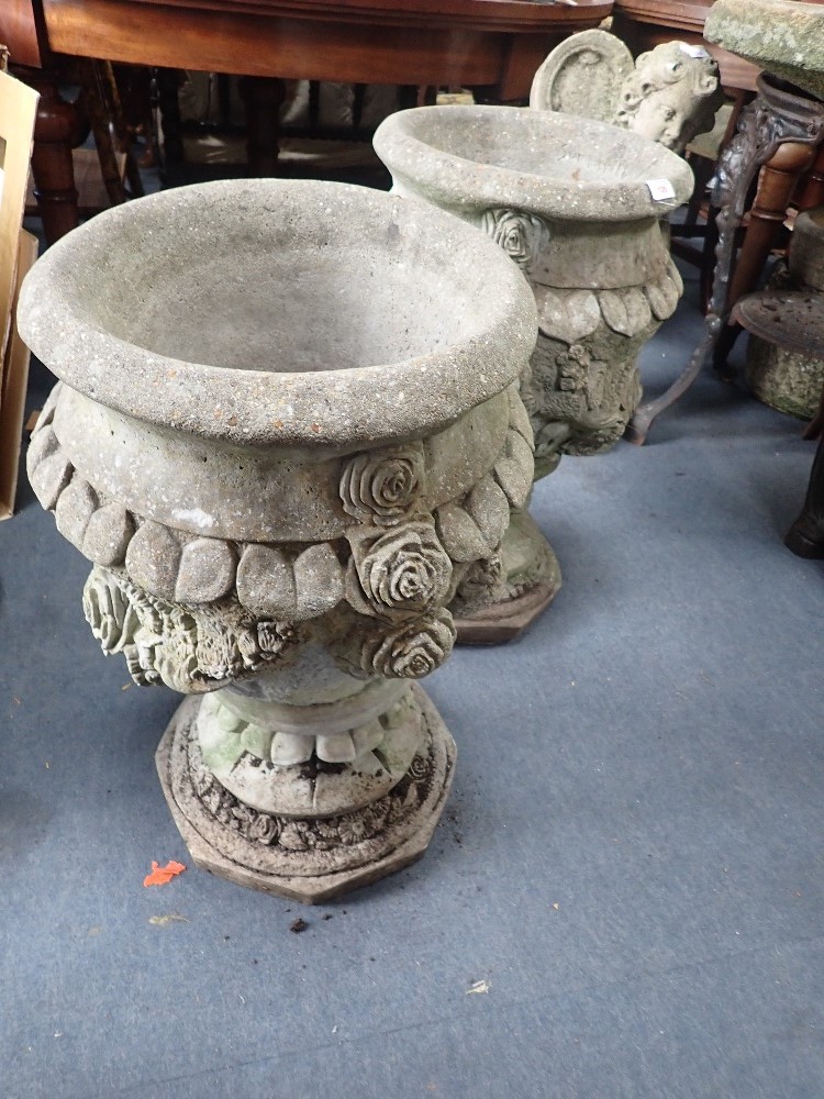 A PAIR OF RECONSTITUTED GARDEN URNS decorated with roses, 65cms high