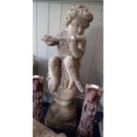 A RECONSTITUTED GARDEN ORNAMENT in the form of a Putto playing a flute sitting on a ball 100cms high