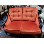 A REPRODUCTION TWO SEATER SOFA with an ebonised frame and bright orange velvet upholstery