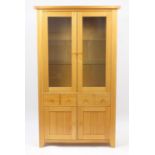 Light oak illuminated display cabinet with a pair of glazed doors above two drawers and a pair of