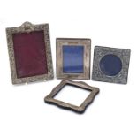 Four silver easel photo frames with embossed decoration, various hallmarks, the largest 18cm x