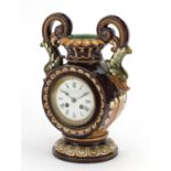 Continental pottery mantel clock in the form of vase with twin dolphin handles, the enamelled dial