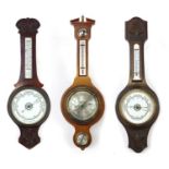 Three carved wall barometers with thermometers comprising two mahogany and one oak, the largest 81cm