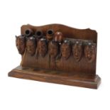 Carved oak devil head design pipe stand with four pipes including two with silver mounts, the rack