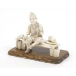 Good Japanese ivory okimono of a man on a bench raised on a rectangular wood plinth base,