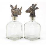 Pair of glass decanters with bronzed giraffe and rhinoceros head design stoppers, each 25cm high