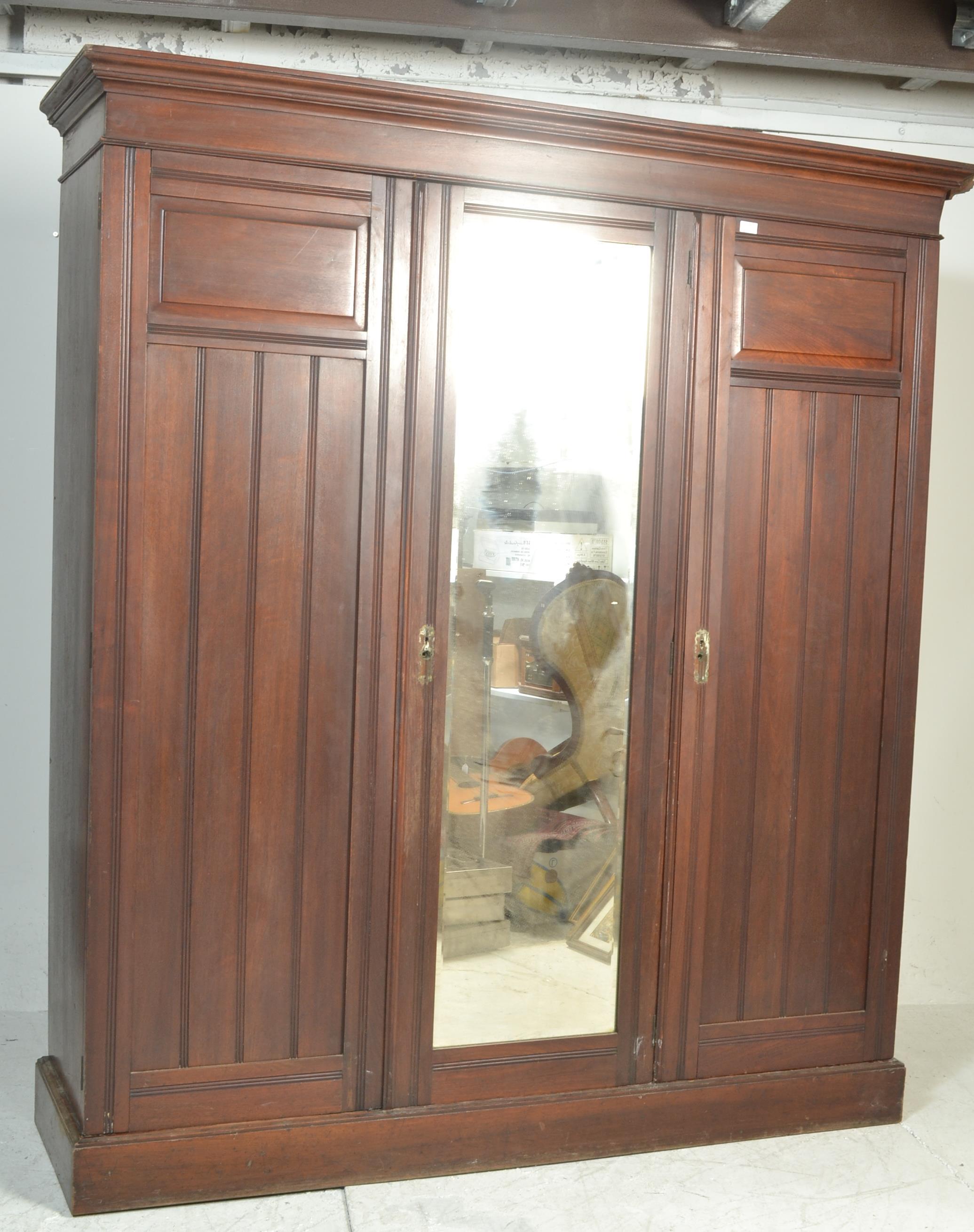 An early 20th Century Edwardian oak triple wardrobe with a central mirrored door flanked by panel