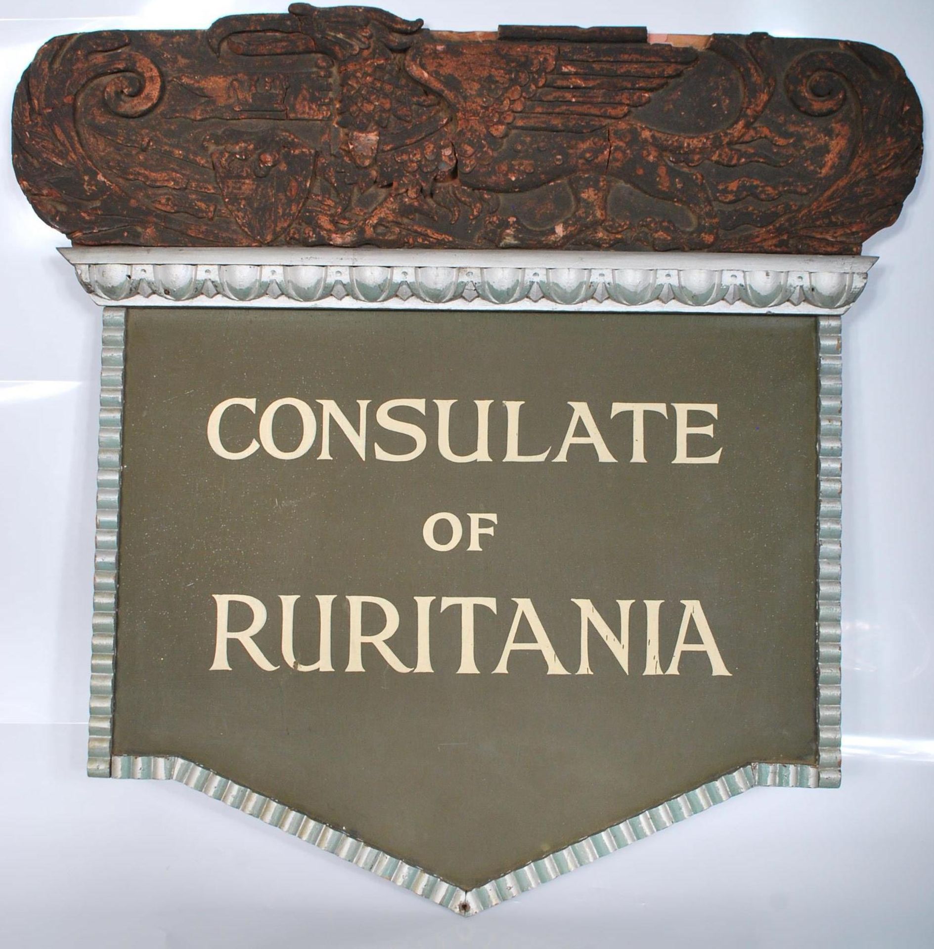 A 20th century shaped wooden sign for the ' Consulate Of Ruritania '. The sign having applied wooden