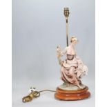 A Capodimonte table lamp in the form of a lady holding a lamb raised on a dark wooden base with a