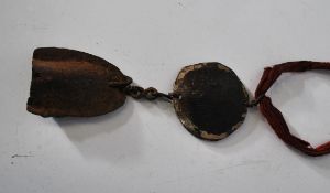 An antique African Tribal metal goats bell suspended by a circular wooden panel attached to red