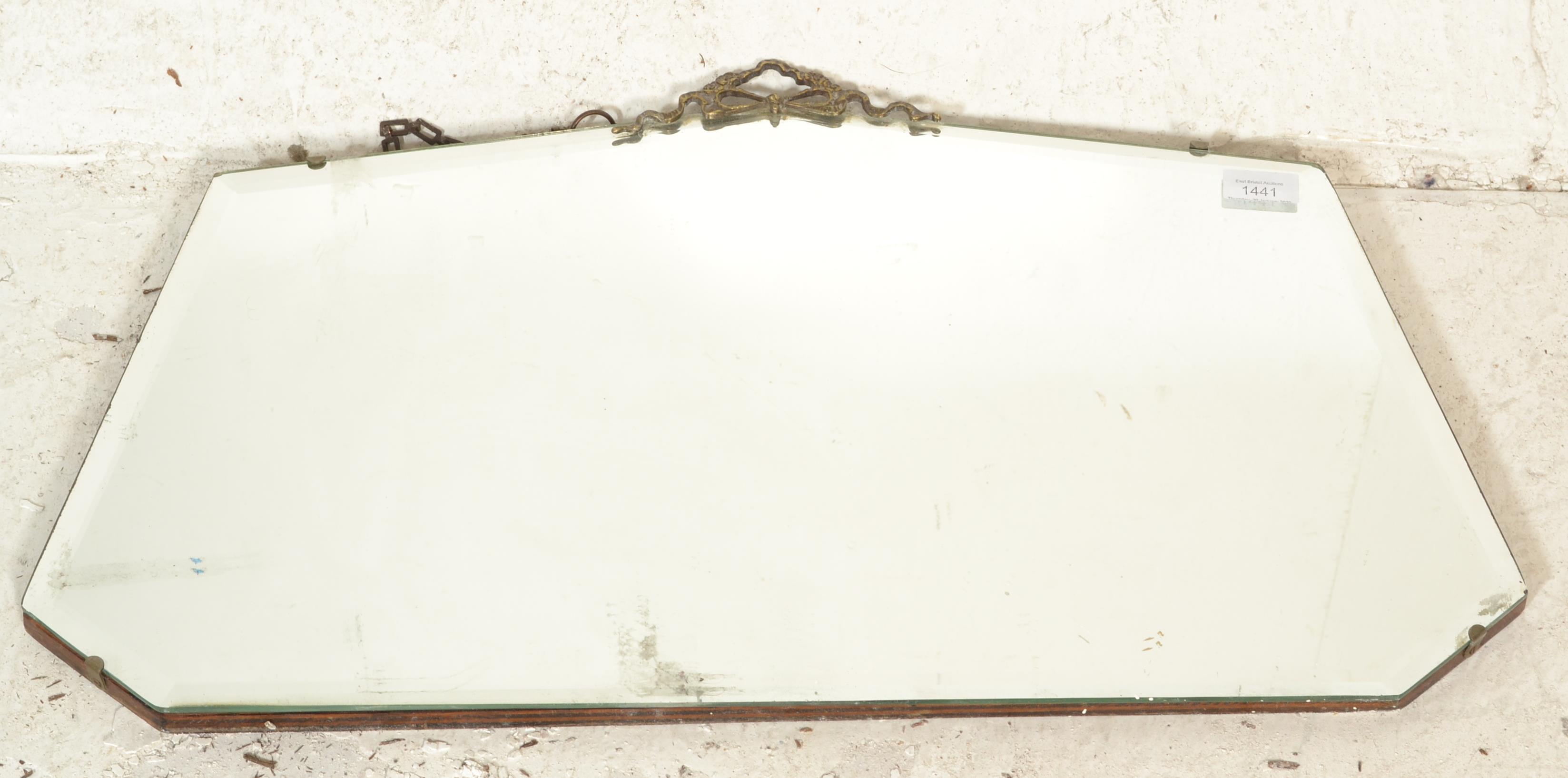 An early 20th Century frameless bevelled edged mirror having decorative brass swag moulded top and