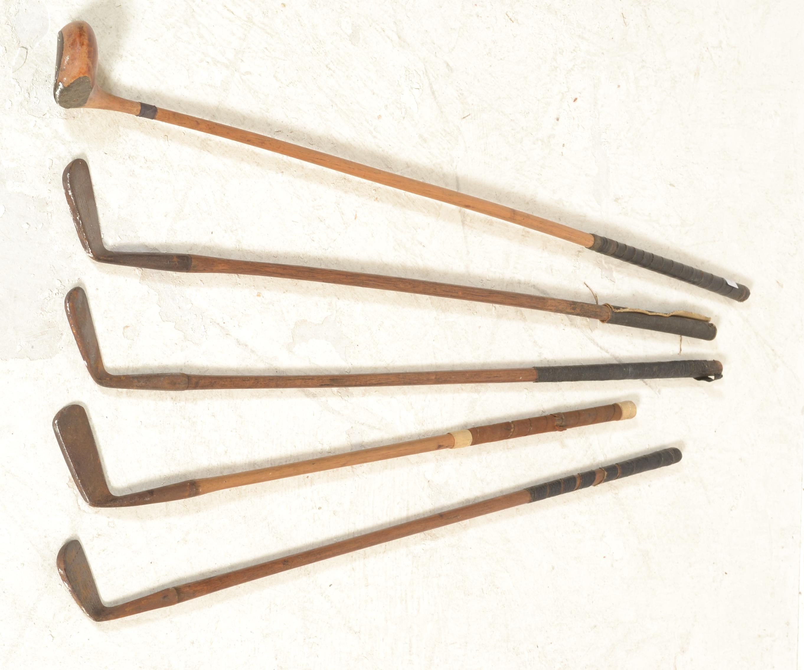 A group of early 20th Century golf clubs having wooden shafts with cast metal heads to include irons