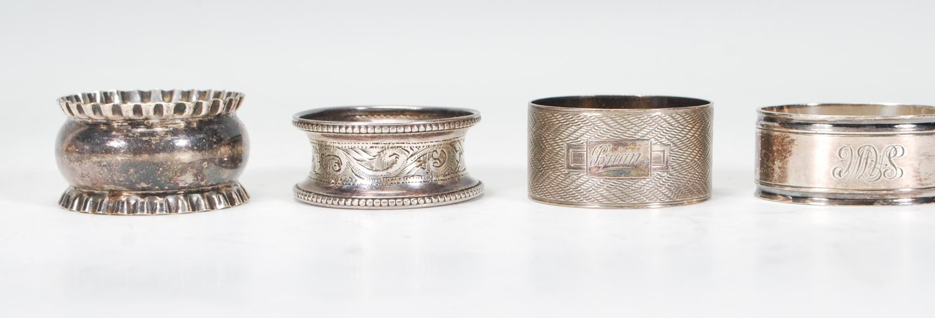 A harlequin set of four silver napkin rings to include an engine turned ring engraved Brian (