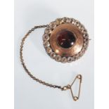 A 19th Century Victorian brooch of round form set with a central red stone cabochon in an engraved
