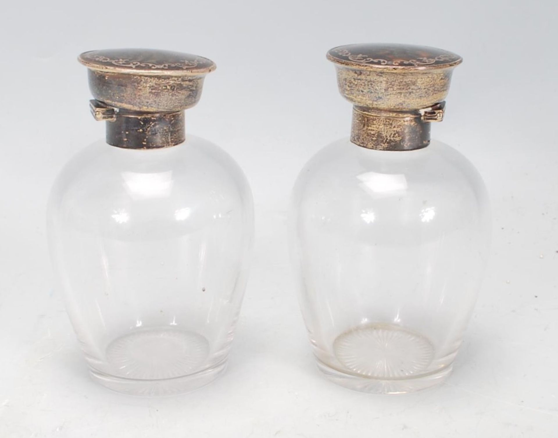 A pair of silver topped dressing table perfume bottles, each lid of round form set with tortoise