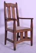 An early 20th Century Arts and Crafts Cotswold school oak carver chair having shaped arm rest.