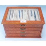 A collection of 20th Century propelling pencils set within a walnut display case with sectional