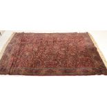A 20th Century Persian Islamic floor rug / carpet having a central red ground panel with floral