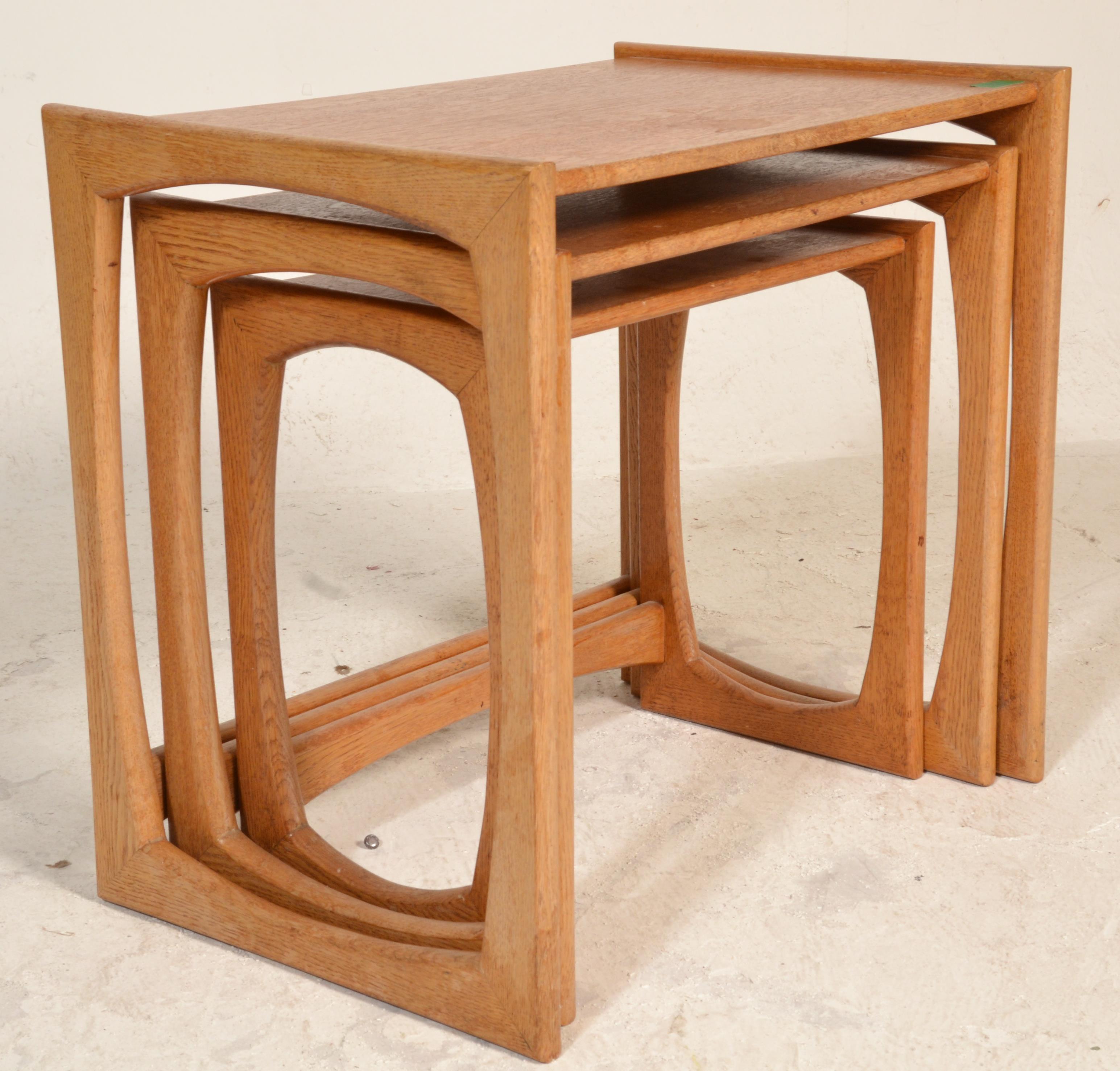 A 1970's G-Plan oak quadrille pattern nest of tables being raised on squared legs with shaped