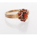 A hallmarked 9ct gold ring having bark effect shoulders set with a cluster of red stones having an