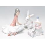 A group of three Lladro ceramic figures to include a young clown boy sitting down with a puppy on