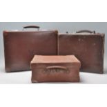 A group of three vintage 20th Century stacking brown leather suitcases having brown leather handles.