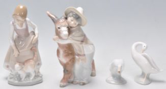 A group of four Lladro figurines a lady with a ginger cat, a boy hugging a donkey and two duck