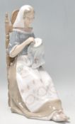 A Lladro figurine in the form of a lady seated doing embroidery. Base stamped Lladro. Measures 28 cm